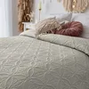 A close-up view of a bed with a beige quilted bedspread and decorative pillows. Produktbild-Vorschau