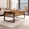 A coffee table is placed on a rug in a living room setting, with a sofa and a chair visible in the background. Voir les images du produit