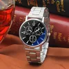A close-up shot of a silver analog watch with a black face, set against a blurred background of books and a glass of red liquid. Produktbild-Vorschau