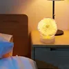 A bedside table with a lamp and a dandelion-shaped night light. Produktbild-Vorschau