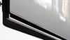 A close-up, angled view of the bottom edge and screen of a modern flat-screen television, likely a smart TV, against a plain white background. Produktbild-Vorschau