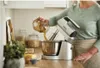 A person is using a hand mixer in a kitchen setting. Produktbild-Vorschau