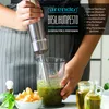 A person is using an immersion blender to make pesto in a glass container, with ingredients like basil, olive oil, and parmesan cheese visible. Produktbild-Vorschau