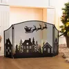 A black metal fireplace screen with a Christmas scene silhouette is placed in front of a fireplace, with a decorated Christmas tree visible to the right. Produktbild-Vorschau