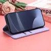 A purple phone case with a phone inside is displayed on a pink surface with flowers in the background. Produktbild-Vorschau