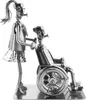 A metal figurine of a caregiver pushing a person in a wheelchair. Voir les images du produit