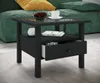 A black side table with a drawer and a shelf is placed next to a green couch with yellow pillows. Voir les images du produit