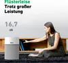 A woman is sitting on the floor next to an air purifier, reaching into a shelf. Produktbild-Vorschau