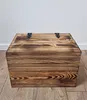 A wooden chest with a lid and metal hinges, placed on a wooden floor against a white wall. Produktbild-Vorschau