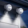 Two white outdoor motion-sensor lights mounted on the exterior of a house at night. Produktbild-Vorschau