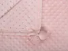 A close-up view of a pink blanket with a textured pattern and pom-pom details. Náhled obrázku produktu