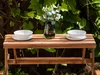 A wooden bench with two bowls and a vase of flowers on it, set against a backdrop of green foliage. Produktbild-Vorschau