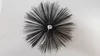 A top-down view of a chimney brush with black bristles radiating outwards from a central silver screw. Produktbild-Vorschau