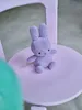 A small lilac bunny plush toy sits on a pink chair. Produktbild-Vorschau