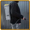 A person wearing a black jacket and jeans stands outdoors, holding a backpack sprayer. Produktbild-Vorschau