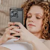 A woman is lying down and looking at her phone, which is in a protective case. Produktbild-Vorschau