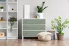 A dresser with green drawers and a woven pouf in front of it, next to a bookshelf, in a room. Produktbild-Vorschau