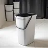 A white plastic trash can with a black lid and handle sits on a marble floor in a kitchen setting. Other similar trash cans are stacked in the background. Anteprima dell’immagine prodotto