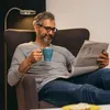 A man is sitting in a chair, reading a newspaper and holding a mug. A floor lamp is behind him. Anteprima dell’immagine prodotto