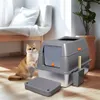 A cat sits next to a modern, enclosed cat litter box with a scoop and a mat in a well-lit room with a plant and a chair. Náhľad obrázku produktu