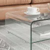 A close-up view of a transparent glass coffee table with a cup of coffee on it, next to a brown leather sofa. Anteprima dell’immagine prodotto