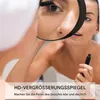 A woman is applying mascara while looking into a magnifying mirror. Produktbild-Vorschau