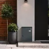 SoBuy Paketbox OGS65-DG von der Seite: geschlossene Tür an Wand neben Holzpaneel und Topfpflanze Vista previa de la imagen del producto