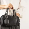 A person is holding a black handbag with an attached black earbud case. Voir les images du produit