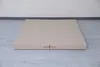 A beige, two-part gymnastics mat is laid flat on a light gray wooden floor, with a white wall in the background. Náhled obrázku produktu
