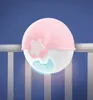 A pink and white baby night light projector is attached to the side of a crib. Náhled obrázku produktu