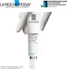 A tube of La Roche-Posay Redermic Retinol Concentrat is held by gloved hands, with marketing text and logos in the background. Podgląd zdjęcia produktu