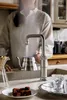 A person is filling a kettle with hot water from a faucet in a kitchen setting. There are also chocolates and coffee brewing equipment visible. Anteprima dell’immagine prodotto