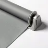 A close-up of a gray roller blind attached to a window frame. Produktbild-Vorschau