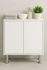 A white cabinet with chrome legs, a soap dispenser, a plant, a bowl, and stacked towels on top, placed against a tiled wall. Produktbild-Vorschau