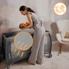 A woman is holding a baby over a travel crib, with a close-up inset showing airflow through the mesh. Produktbild-Vorschau
