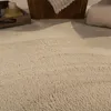 A close-up view of a beige, shaggy rug with a woven basket and a cushion in the background. Produktbild-Vorschau