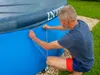 A man is kneeling and securing a cover onto an inflatable pool. Produktbild-Vorschau