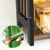 A close-up view of a black wooden shelf unit with a glass jar filled with chips and a detail of bamboo stalks. Produktbild-Vorschau