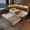 A modern bedroom with a grey upholstered bed featuring a pull-out trundle bed, integrated shelving with LED lighting, and a large window overlooking a city skyline. Náhled obrázku produktu