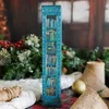 A decorative advent calendar designed to look like a bookshelf, set against a festive, slightly blurred background with greenery and berries. Náhled obrázku produktu