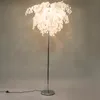 A floor lamp with a white, leaf-like shade stands against a gray background. Produktbild-Vorschau