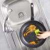 A frying pan with food residue is being scrubbed with a green sponge in a kitchen sink. Náhled obrázku produktu