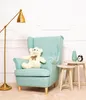 A teddy bear sits in a light blue armchair next to a gold floor lamp and small side tables with decorative items. Voir les images du produit