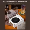 A white retro-style Bluetooth speaker resembling a record player is shown on a wooden table, with a glass of whiskey and a newspaper nearby. Produktbild-Vorschau