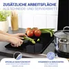 A person is chopping vegetables on a glass cutting board placed on a stovetop. Tomatoes and green onions are also on the board. A pot is visible to the right. Produktbild-Vorschau