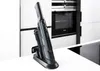 A cordless handheld vacuum cleaner is shown in its charging dock on a kitchen counter. Náhled obrázku produktu
