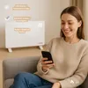 A woman is sitting on a couch and using her smartphone while a white electric heater is in the background. Voir les images du produit