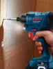 A hand is holding a Bosch impact driver and screwing a screw into a wooden surface. Anteprima dell’immagine prodotto