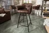 A bar area with a leather bar stool in the foreground and other bar stools and furniture in the background. Produktbild-Vorschau