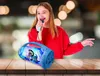A young girl is singing into a microphone, with a blue Bluetooth speaker featuring Disney's Stitch character in front of her. Voir les images du produit